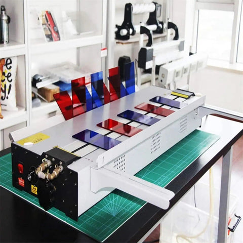 Rock Solid Electric Plastic Hot Bender And Acrylic Bending Press With Adjustable Heat Settings And Fast Chill Water Cooling For Perfect Pvc Angles And Knockout Storefront Displays on a work table with colored acrylic sheets.