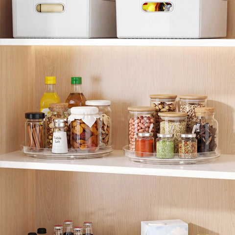 Nine Inch Clear Lazy Susan Set Of Two Round Rotating Turntable Organizers With Non Slip Base For Pantry Cabinet And Fridge Shelf organizing spices and snacks in jars on a shelf.