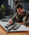 Man assembling Fighter Jet Building Set 33038 B2 Stealth Bomber Model Kit For Adults And Military Fans on a wooden table.