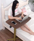Rock Solid Mobile Laptop Desk With Fully Adjustable Rolling Casters Top Tier Portable Workstation in use beside a bed.