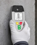 6-in-1 Stud Finder Wall Scanner Metal Detector LCD Display(Grey) held in hand against a concrete wall, showing bright LCD interface.