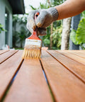 Hand applying Premium Weatherproof Wood Stain With Semi Gloss Walnut Finish For Indoor And Outdoor Use on wooden planks.