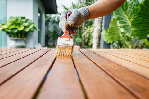 Hand applying Premium Weatherproof Wood Stain With Semi Gloss Walnut Finish For Indoor And Outdoor Use on wooden planks.
