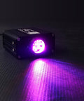 Compact 16W RGBW Fiber Optic Light Engine With Twinkle And Sound Activated Modes on black surface, purple light beam