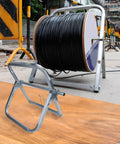 Heavy Duty Steel Cable Reel Dispenser Rack Delivers Tangle Free Cord Management With Smooth Rolling Base on job site with black cable.