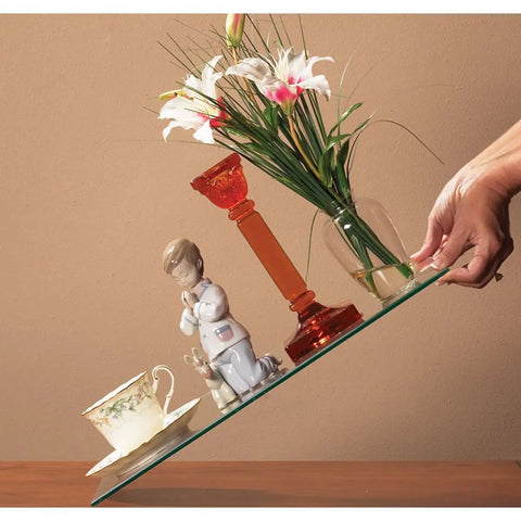 Hand holding slanted glass shelf with items secured by Removable Museum Putty For Securing Antiques And Collectibles, Non Toxic Reusable Adhesive For Surfaces And Furniture, Neutral Cream White, 2.64 Ounce Pack, Roll It In Your Hands Until Soft Then Apply To Base Of Items.