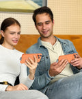 Couple using smartphones together on a couch, holding phones with orange cases in a cozy indoor setting.