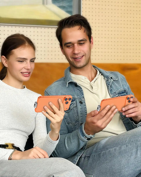 Couple using smartphones together on a couch, holding phones with orange cases in a cozy indoor setting.