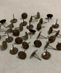 Hardcore Upholstery Tacks And Furniture Nails 100 Pack Heavy Duty Decorative Hardware Big Time Upgrade For DIY Restorations Solid Antique Brass, shown from angled view.