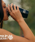 Person drinking outdoors from a black 24 oz insulated stainless steel tumbler with a lid