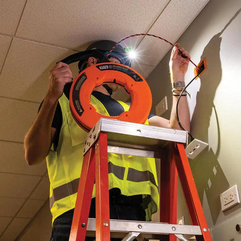 High Flex 75 Foot Tri Strand Polyester Fish Tape For Smooth Electrical Wire Pulling used by a worker on a ladder with headlamp.