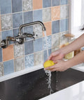Person washing a lemon under a Kitchen Wall Faucet With Two Cross Handles In Brushed Nickel Finish Wall Mounted And Adjustable Spread