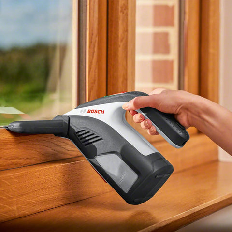 Side view of Bosch GlassVAC handheld battery window vacuum cleaner in gray/black, used on a window.