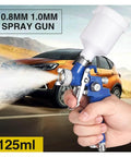 Pro Level Pneumatic Paint Spray Gun With One Millimeter Nozzle in hand spraying a mist, showing the clear fluid jar and controls.