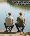 Two people fishing sitting on Lightweight Travel Folding Tripod Camping Stool Portable Chair 14.6 Inch Seat Holds Up To 210 Lbs by a lake.