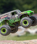 Grave Digger 1 To 18 Scale Mini LMT 4X4 RC Monster Truck RTR with green body and LED headlights performing a jump outdoors