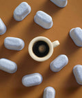 12 blue charcoal water filters for Breville espresso machines arranged around a white coffee cup, top-down view