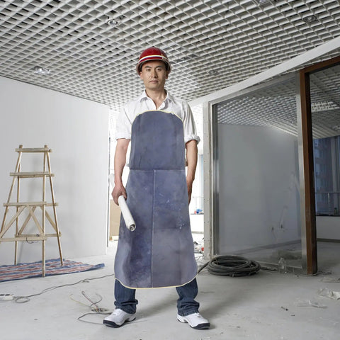 Person wearing Pro Grade Cowhide Welding Apron Heat Resistant Shield For Sparks And Splatter in a construction site holding blueprints.