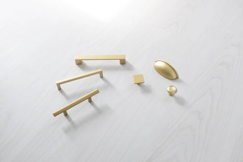 Assorted gold cabinet handles and knobs on white surface