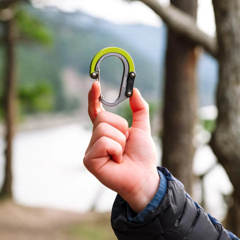 Hand holding HeroClip Small Carabiner Clip And Hook Three In One For Purses Strollers And Backpacks Stealth Black in outdoor setting