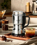 Top Shelf Electric Coffee Grinder And Spice Mill Featuring A Hella Quick 150 Watt Motor Plus Razor Sharp Stainless Steel Blades For Roasted Beans Fresh Herbs Whole Spices And Nuts Boss Cleaning Kit Included on a wooden tray with coffee beans and a drink.