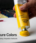 Hand squeezing yellow oil paint from tube onto canvas, demonstrating impasto technique.