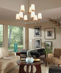 Living room with modern chandelier, beige sofas, framed art, and large windows overlooking trees.
