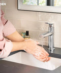 Person washing hands under Meena Chrome One-Handle Bathroom Sink Faucet With Single Hole Mount And Optional Deckplate Drain Assembly Slick