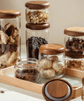 Four Piece Glass Storage Jars With Airtight Wooden Lids Wide Mouth Canister Set filled with snacks and coffee on a wooden tray.