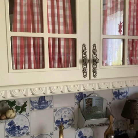 Antique Bronze Vintage Style Cabinet Knobs Set on white kitchen cabinet with red checkered curtains and decorative tiles.