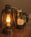 Pack Of 2 Vintage Rustic Lantern Lamps With Edison LED Bulbs, Bronze Rust Finish on a wooden table next to coffee machine.