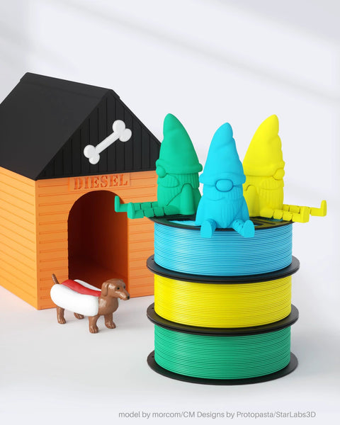 Three colored PLA filament spools for 3D printers in blue, yellow, and green, stacked beside a toy dog and doghouse.