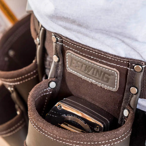 Close-up of a heavy duty leather tool apron with seven pockets, hammer holder, and rivet reinforced edges for pro grade toughness.