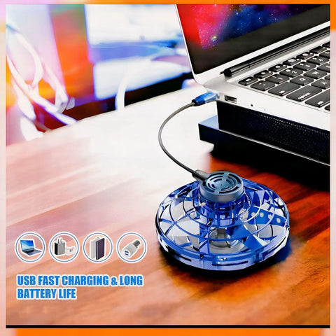Hand Operated Mini Drone Orb With LED Lights UFO Magic Flying Spinner Hand Controlled Hover Boomerang Toy For Kids Teens 7 Plus Indoor And Outdoor Play Blue Small charging via USB next to laptop on table.