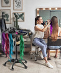 Hairstylist Rolling Cart For Salon Pros With Secure Storage Platform Hair Separator Stand And Color Tray With Dye Bowls And Tools Durable Metal Trolley On Wheels Black in a salon setting next to hairstylist and client.