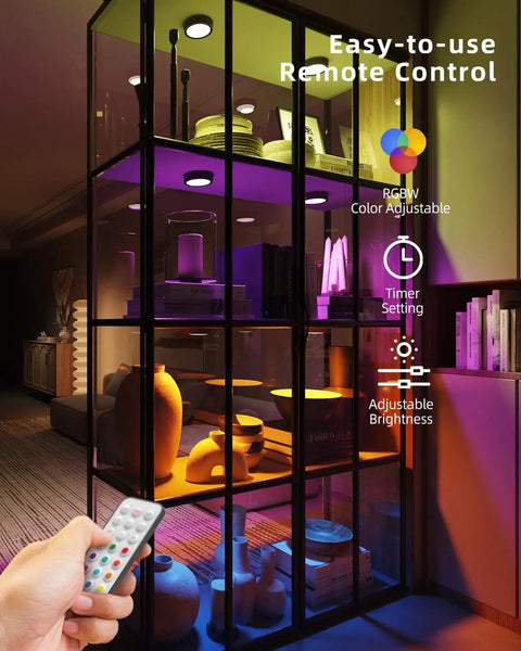 Motion Sensor Puck Lights With Remote No Fuss 2400mAh Rechargeable RGBW Wireless Under Cabinet Lighting Kit illuminating a glass shelf.
