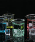 Four colored 100 ml glass beakers filled with liquid on black surface, part of the Twenty Pack 100 Milliliters Glass Beakers Set, Heavy Duty Borosilicate Lab Beakers With Printed Measurements, Bulk Quantity For Lab Or Classroom Or Home Science Projects.