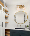 Bathroom with two light gold vanity light with clear glass shades, modern decanter style fixture, mirror, and sink.