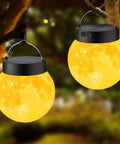 Lit 3D Moon Globe Solar Garden Lights 2 Pack With Warm White LEDs glowing at night hanging outdoors