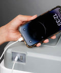 Person plugging a smartphone into the USB port of a Massive 30L Electric Travel Cooler For Cars And Rvs 12V DC Portable Refrigerator.