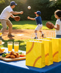 Softball Themed Paper Goodie Bags With Handles 12 Pack for Party Favors on picnic table, kids playing softball in background.