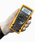 Gloved hand holding ESFP True RMS Digital Multimeter For Pro Troubleshooting Delivers True RMS AC And DC Voltage And Current Readings