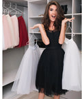 Woman smiling holding white dresses in a clothing store with hanging skirts and modern display shelves.