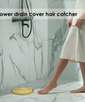 Gold Stainless Steel Shower Drain Catcher With Soft Silicone Edge Flat Round Tub Strainer placed in a bathroom with a woman stepping over it.