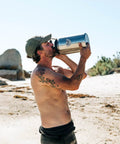 Man drinking from Rambler Gallon Jug Vacuum Insulated Stainless Steel Water Bottle With MagCap at the beach