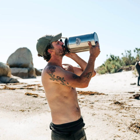 Man drinking from Rambler Gallon Jug Vacuum Insulated Stainless Steel Water Bottle With MagCap at the beach