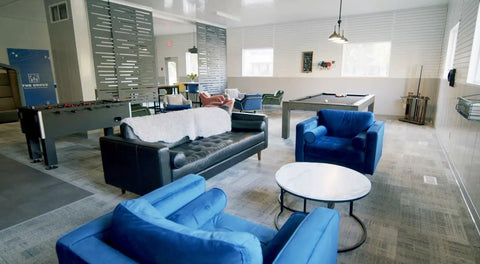 Modern lounge area with blue and black seating, a foosball table, pool table, and white walls showing interior layout.