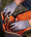 Person wearing Klein Tools safety gloves reaching into a tool bag outdoors.