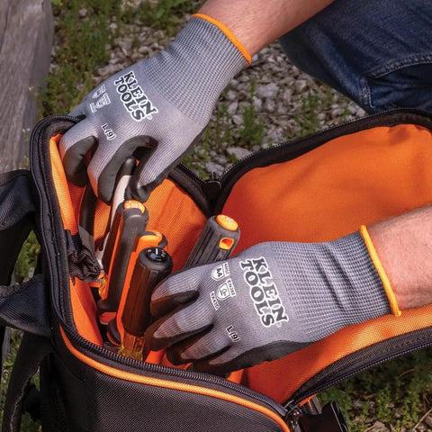 Person wearing Klein Tools safety gloves reaching into a tool bag outdoors.