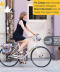 Person on white bicycle with colorful bags, Po Campo brand label visible, industrial setting, clear sky and door background.